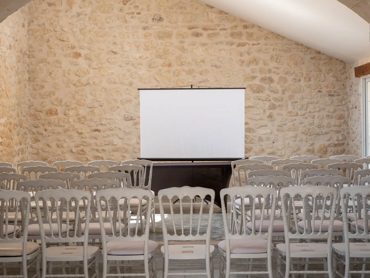 Écran de projection et rangs de chaises dans la salle en pierre